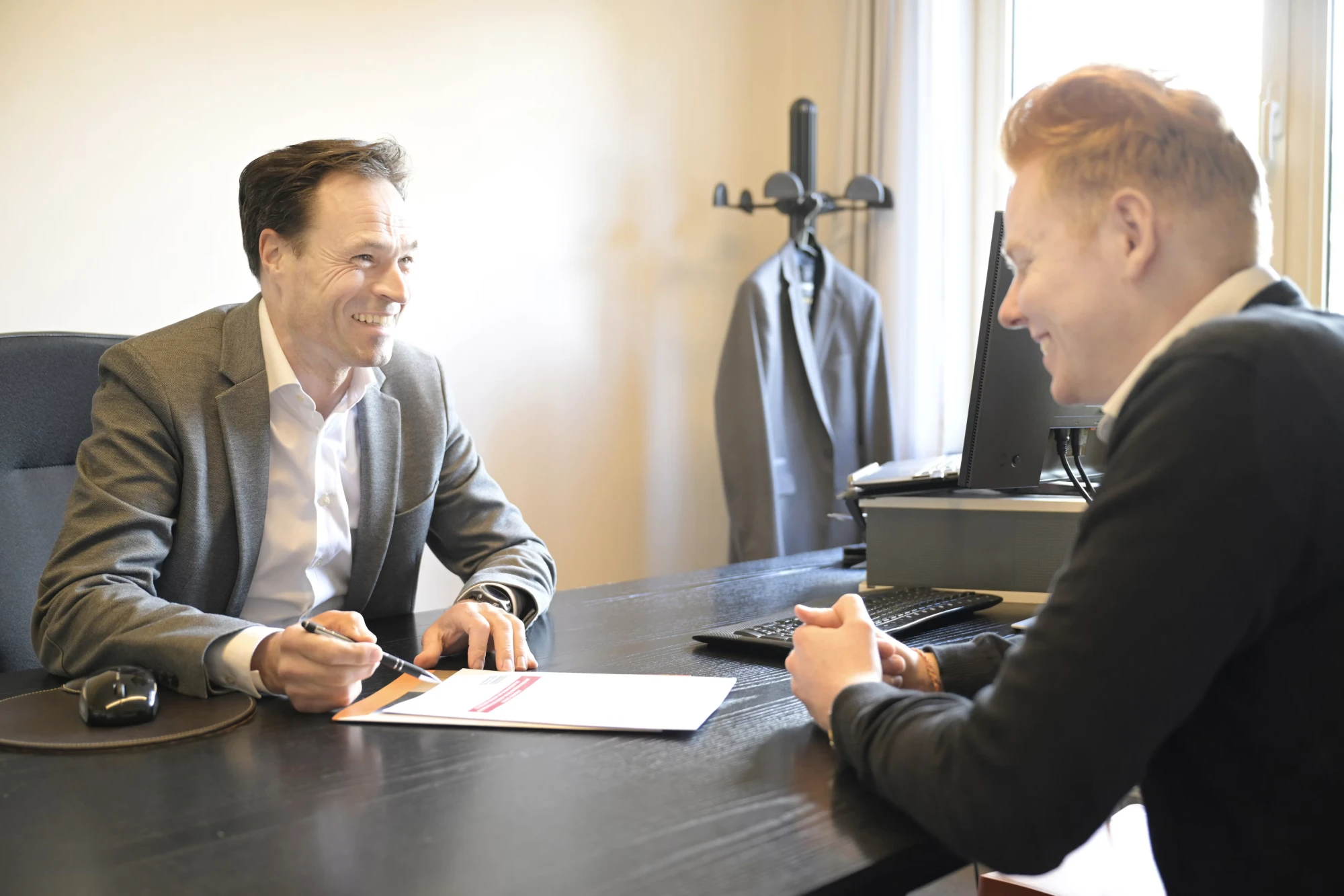 Deux personnes échangent en souriant autour d’un document, à un bureau